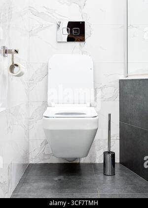 Moderne Toilettenschüssel mit eingebautem Wassertanksystem. Weiße Marmorfliesen an den Wänden und moderner grauer Boden. Stockfoto