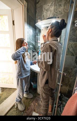 Eine Mutter und Tochter teilen sich einen unbeschwerten Moment im Badezimmer, während sie sich die Zähne putzen, in gemütlicher Kleidung gekleidet und sich auf den Tag vorbereiten Stockfoto