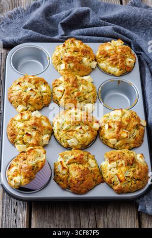 Nahaufnahme von herzhaften Zucchini Feta Muffins in Muffindose auf rustikalem Holztisch mit Küchentuch, vertikale Ansicht von oben, nicht KI generiert Stockfoto