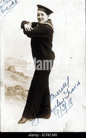 Pauline Travis, eine männliche Imitatorin, die 1918 aktiv war, wird in diesem schwarz-weißen Studio-Porträt dargestellt, das eine Matrosenuniform und eine Kappe trägt, die die Aufschriften „R.N.“ und „V.R.“ trägt. Ihre selbstbewusste Pose, die Arme gekreuzt und lächelnd, spiegelt den theatralischen Bravado wider, der typisch für edwardianische Varieté-Acts ist. Eine malerische Kulisse am Meer und ihre handgeschriebene Inschrift („Yours aufrichtig, Pauline Travis, 9/3/18“) sorgen für Intimität und Flair. Als Darsteller im Argyle Theatre of Variations in Birkenhead verkörperte Travis die Widerstandsfähigkeit und das Geschlechterspiel auf der populären Bühne. Stockfoto