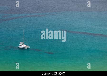 Gozo, Malta - 23. Juni 2021: Ein weißer Katamaran segelt auf türkisfarbenem Wasser des Mittelmeers in der Nähe der Insel Gozo. Stockfoto