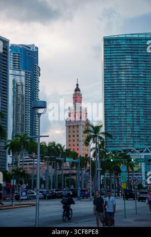 Freedom Tower in der Innenstadt von Miami in der Abenddämmerung, umgeben von modernen Wolkenkratzern und Palmen, mit Fußgängern und Verkehr im Vordergrund. Stockfoto