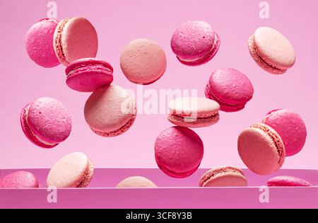 Viele französische Erdbeer-Macarons fallen in die Kiste auf rosa Hintergrund. Stockfoto
