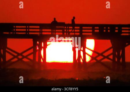 Isle Of Palms, Usa. August 2025. Die Menschen auf der Isle of Palms Angelpier sind vom Sonnenaufgang über dem Atlantik am Front Beach, 21. August 2025 in Isle of Palms, South Carolina, umgeben. Die Sonne scheint zu verschwinden, als sie am Horizont in eine Bank von schweren Wolken aufsteigt. Quelle: Richard Ellis/Richard Ellis/Alamy Live News Stockfoto