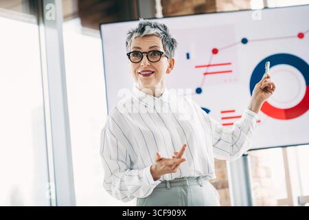 Selbstbewusste, reife Geschäftsfrau, die Datenanalysen während eines Unternehmenstreffens in einem modernen Büroumfeld vorstellt Stockfoto