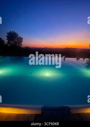 Der beleuchtete Infinity-Pool reflektiert einen lebhaften Sonnenuntergang über den toskanischen Hügeln in Rapolano Terme, Italien, und schafft eine entspannende und luxuriöse Atmosphäre Stockfoto