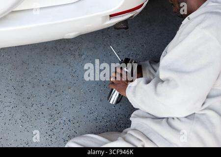 Ein afroamerikanischer Mann installiert eine verchromte Auspuffspitze auf Ein Fahrzeug Stockfoto