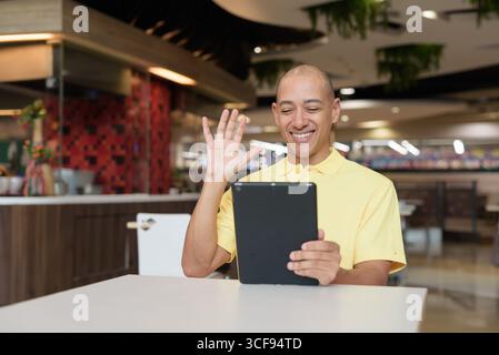 Porträt eines Reifen italienischen Mannes, der drinnen in einem modernen Restaurant sitzt und einen digitalen Tablet-Computer verwendet, der ferngesteuert arbeitet Stockfoto
