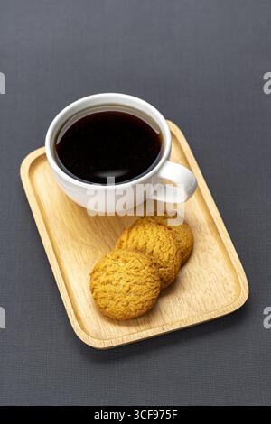 Schwarzer Kaffee mit drei Plätzchen auf Holztablett, minimalistischer Stil, auf dunklem Hintergrund, warm und einladend, perfekt zum Frühstück oder Snack Stockfoto
