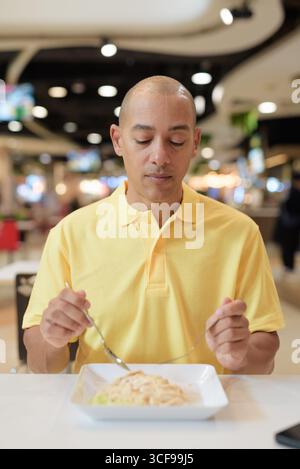 Porträt eines Reifen italienischen Mannes, der drinnen in einem modernen Restaurant sitzt und gesunden Hainanesischen Hühnerreis isst. Stockfoto