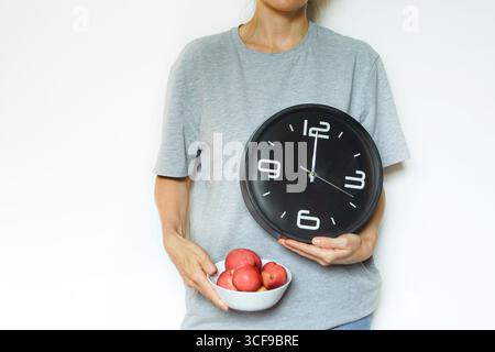 Frau, die eine Uhr und eine Schüssel frischer Nektarinen hält, symbolisiert intermittierendes Fasten, Essensplanung und gesunde Ernährung. Zeitbeschränktes Essen Stockfoto