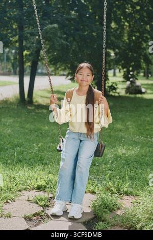 Porträt eines jungen asiatischen Mädchens, das auf Swing sitzt und im Park draußen lächelt Stockfoto