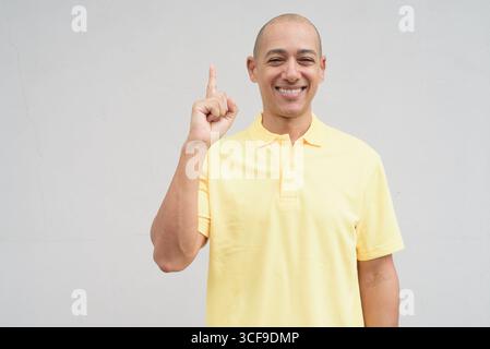 Studio-Porträt eines gutaussehenden, reifen Italieners mit rasiertem Kopf in gelbem Poloshirt, der vor einer neutralen, weißen Wand mit Kopie steht Stockfoto