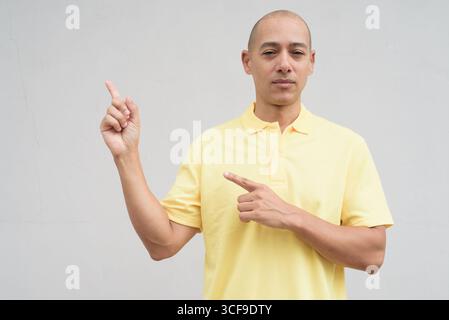 Studio-Porträt eines gutaussehenden, reifen Italieners mit rasiertem Kopf in gelbem Poloshirt, der vor einer neutralen, weißen Wand mit Kopie steht Stockfoto