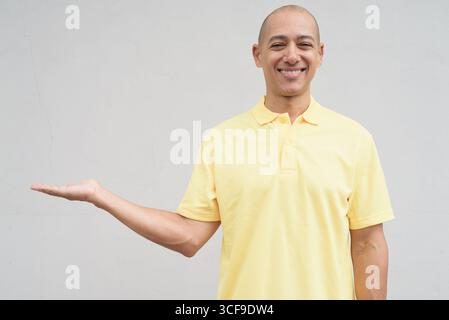 Studio-Porträt eines gutaussehenden, reiferen Italieners mit einem rasierten Kopf, der gelbes Poloshirt trägt, vor einem neutralen, einfarbigen weiß steht Stockfoto