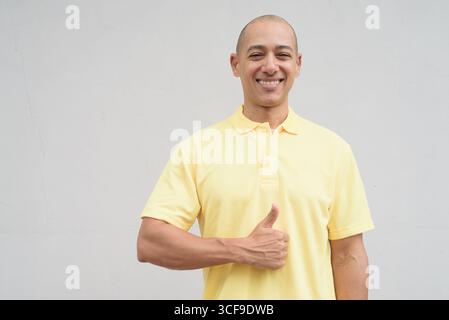Studio-Porträt eines gutaussehenden, reiferen Italieners mit einem rasierten Kopf, der gelbes Poloshirt trägt, vor einem neutralen, einfarbigen weiß steht Stockfoto