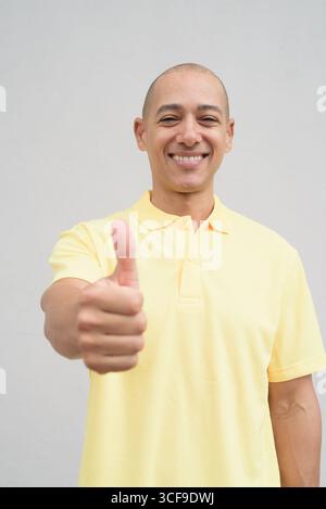 Studio-Porträt eines gutaussehenden, reiferen Italieners mit einem rasierten Kopf, der gelbes Poloshirt trägt, vor einem neutralen, einfarbigen weiß steht Stockfoto