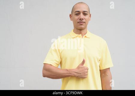 Studio-Porträt eines gutaussehenden, reifen Italieners mit rasiertem Kopf in gelbem Poloshirt, der vor einer neutralen, weißen Wand mit Kopie steht Stockfoto