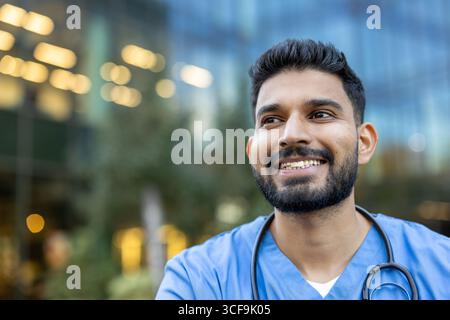 Gesundheitspersonal in Schutt lächelt draußen, stellt Positivität und Professionalität vor einem zeitgenössischen Gebäudehintergrund dar. Stockfoto