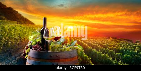 Wein - Weingläser Mit Flaschen Und Trauben Auf Barrel In Vineyard - Ländliche Landschaft Bei Sonnenuntergang Stockfoto