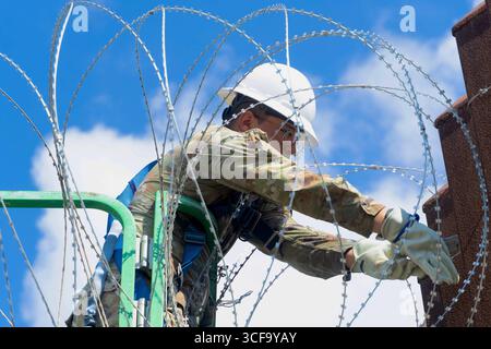 Brownsville, Usa. August 2025. Texas National Guardsmen, die unter der Joint Task Force-Southern Border arbeiten, installieren am 12. August 2025 in der Nähe von Brownsville, Texas, eine Drahtseile entlang der südlichen Grenzmauer zu Mexiko. Die Soldaten wurden von Präsident Trump zur Unterstützung der Operation Lone Star an die Grenze geschickt. Gutschrift: SSgt. Derek Gutierrez/US Air Force Photo/Alamy Live News Stockfoto