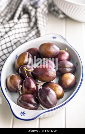 Reife Pflaumen in einer Schüssel auf einem weißen Tisch. Stockfoto