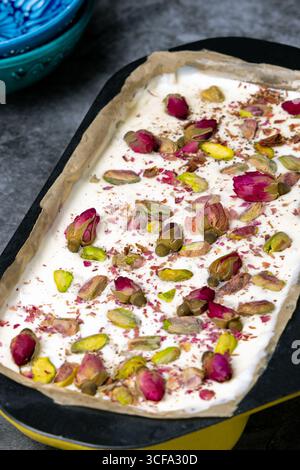 Safran-Eistablett mit getrockneten Rosenknospen, Pistazien und Schokolade – luxuriöses persisches Dessert mit kräftigen Farben und Texturen. Stockfoto