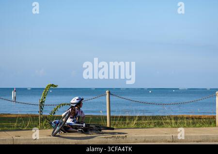 Müde weibliche Fahrradfahrerin, die während der Fahrt im Honolulu Century 2005 auf dem Bürgersteig ruhte, Hawaii Kai, Oahu, Hawaii, USA Stockfoto