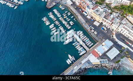 Eingebettet an der Küste erwacht ein malerischer Hafen bei Sonnenuntergang zum Leben, mit Booten, die sanft im türkisfarbenen Wasser wippen, umgeben von lebhaften Strukturen Stockfoto