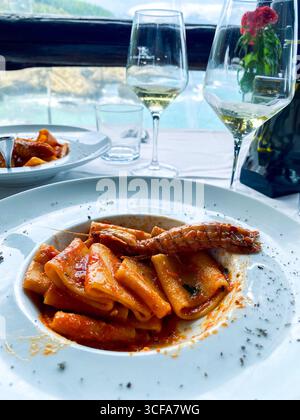 Köstliches Paccheri-Pasta-Gericht mit Mantis-Garnelen und Tomatensauce, serviert auf einem Tisch mit Weingläsern, mit Blick auf das Meer der Abruzzen in Italien Stockfoto