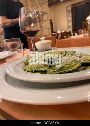 Teller Ravioli mit Pesto und geriebenem Käse in einem eleganten italienischen Restaurant in Pretoro, Abruzzen, serviert. Ein Kellner gießt Wein im Hintergrund Stockfoto