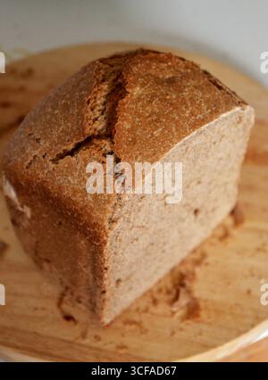 Hausgemachtes dunkles Vollkornweizen-Sauerteigbrot, gebacken in einer Brotmaschine, auf einem Schneidebrett. Ein modernes und gesundes Backergebnis. Stockfoto