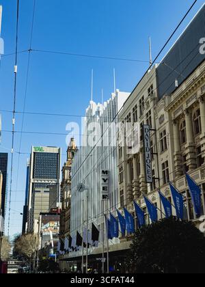 Blick auf Melbournes Bourke Street Mall mit Myer- und David Jones-Gebäuden, die historische und moderne Architektur unter einem klaren blauen Himmel verschmelzen. Stockfoto