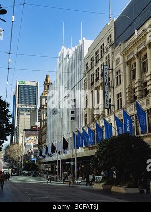 Blick auf Melbournes Bourke Street Mall mit Myer- und David Jones-Gebäuden, die historische und moderne Architektur unter einem klaren blauen Himmel verschmelzen. Stockfoto