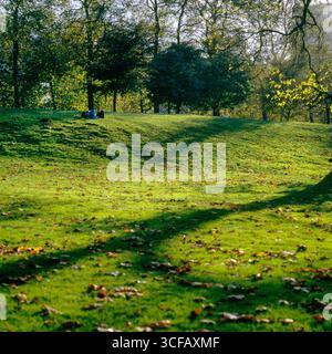 Menschen, die auf einem grasbewachsenen Hügel in Green Park, City of Westminster, London, England, Großbritannien liegen Stockfoto