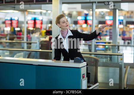 Weiße Dame Check-in-Agentin, die Passagiere mit Scanner direkt auf den belebten Flughafenschalter zeigt Stockfoto