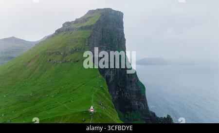 Hoch aufragende Klippen mit üppigem Grün überblicken den Atlantischen Ozean und bieten atemberaubende natürliche Schönheit. Ein kleiner Leuchtturm deutet auf die maritime Geschichte hin Stockfoto