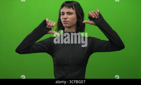 Die junge hispanische Frau in schwarzer Sportkleidung zeigt in hellgrünem Studio eine Geste mit doppeltem Daumen nach unten; Ablehnung negativem Objekt Stockfoto