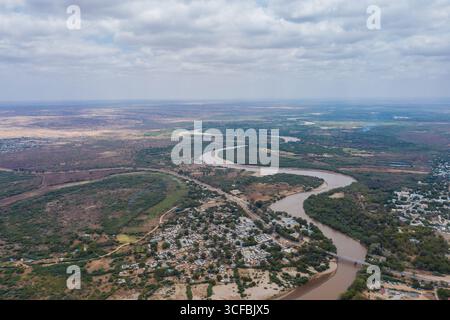 Aus der Vogelperspektive auf den Fluss Tana, der sich durch die karge Landschaft schlängelt und durch die karge grüne Vegetation und Infrastruktur schneidet, Garissa, Kenia. Stockfoto