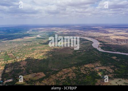 Aus der Vogelperspektive auf den Fluss Tana, der sich durch die grüne und gelbe Landschaft unter einem bewölkten Himmel schlängelt, Garissa, Kenia. Stockfoto