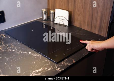 Finger und Hand eines Mädchens, das einen Kinderschutz auf einem modernen Keramikkochfeld installiert Stockfoto