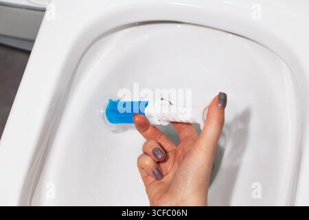 Eine Spritze mit ozeanduftendem Gel zur Reinigung und Desinfektion der Toilette in einer Hand vor dem Hintergrund einer Toilette. Antibakterielle Wirkung Stockfoto