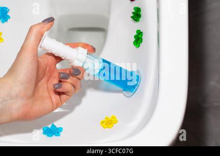Eine Spritze mit ozeanduftendem Gel zur Reinigung und Desinfektion der Toilette in einer Hand vor dem Hintergrund einer Toilette. Antibakterielle Wirkung Stockfoto