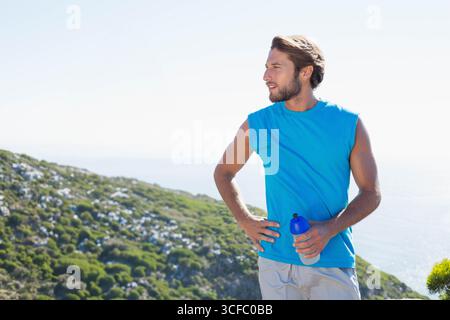 Mann in seinen 30ern, der auf einem Hügel an der Küste steht und mit blauer Wasserflasche, Kopierraum trainiert Stockfoto