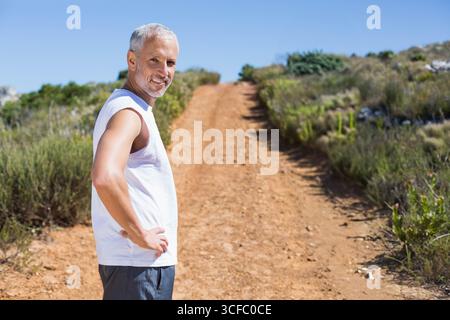 Senior Mann, der Hände auf Hüften auf einem roten Wanderweg auf felsigem Hügel steht, Kopierraum Stockfoto