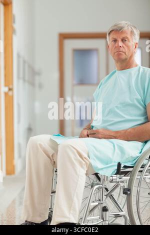 Seniorenmann sitzt im Rollstuhl mit grünem medizinischem Kleid im Krankenhausflur, Kopierraum Stockfoto