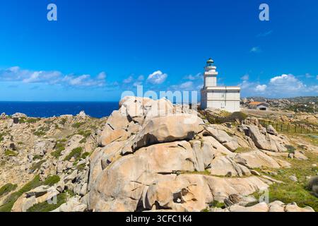 Weißer Leuchtturm in Capo Testa, Sardinien, umgeben von zerklüfteten Granitfelsen, Küstenvegetation und tiefblauem Meer unter einem klaren sonnigen Himmel. Stockfoto