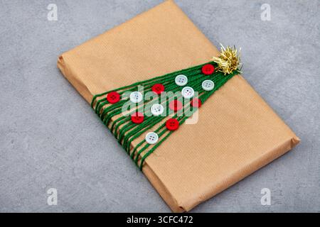 Braunes Geschenkpapier mit einem Weihnachtsbaum aus Knöpfen und Schnur. Der Baum besteht aus grünem Schnur mit weißem und rotem Knopf Stockfoto
