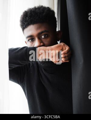 Zugeschnittenes Bild eines traurigen schwarzen Mannes. Lockiger junger bärtiger Kerl in Depression und Blick auf die Kamera. Person trägt schwarzen Pullover Stockfoto