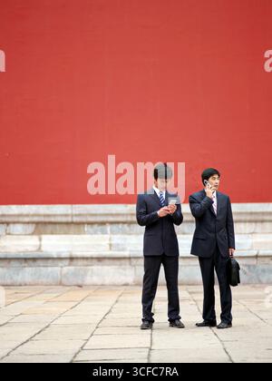 Zwei chinesische Geschäftsleute in Anzügen, die Dokumente halten, am Telefon eine Diskussion führen Stockfoto